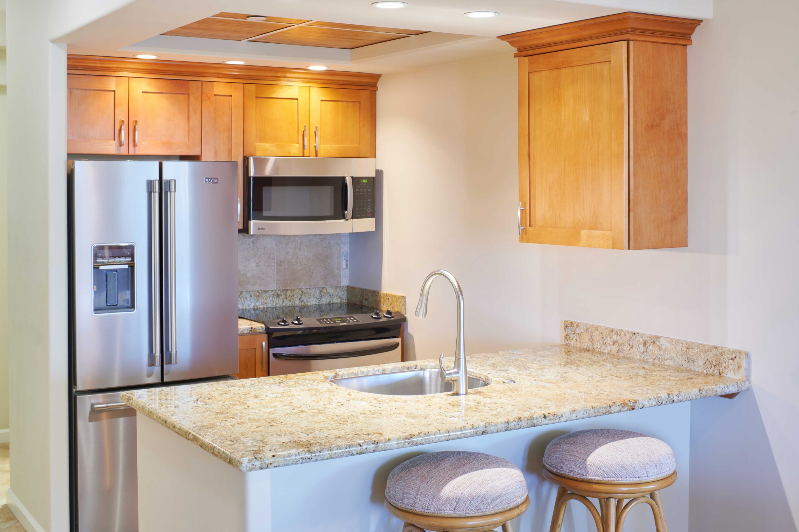 Studio garden view kitchen with fridge, microwave, cabinets, and bar stools