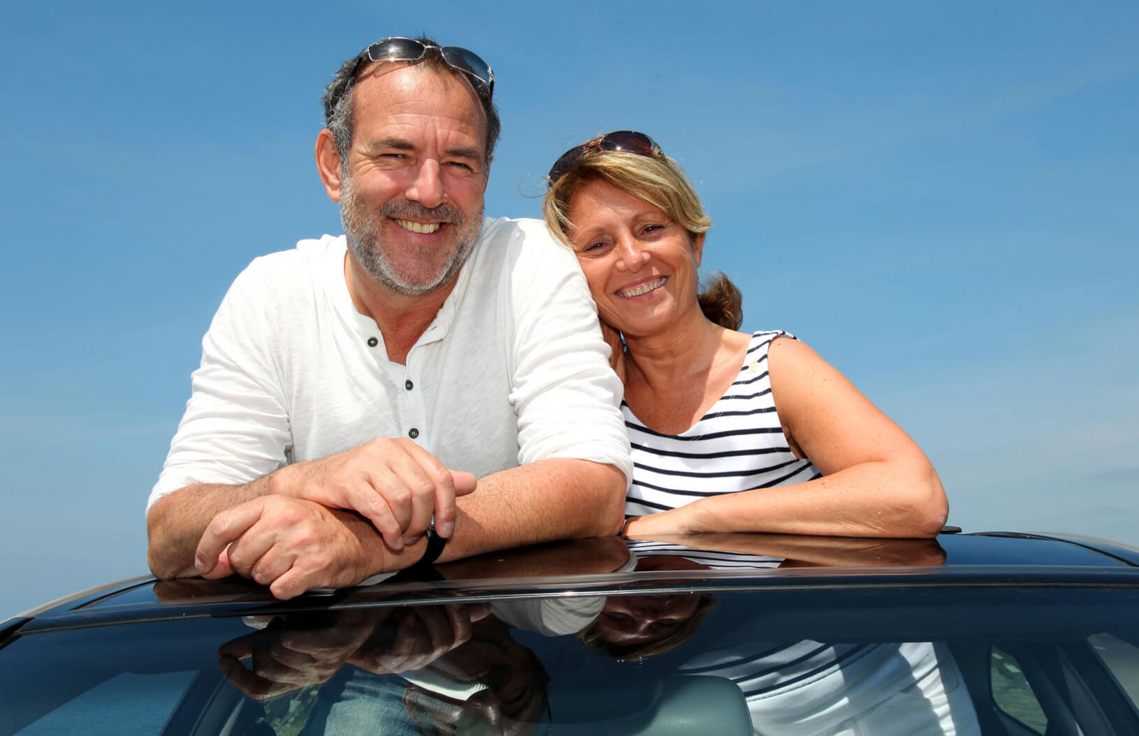 A man and woman standing in the sunroof of their car.