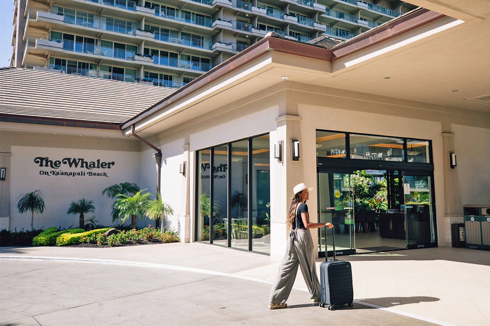 Woman walking through port cochere with luggage.